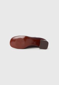 Brown heeled shoe with smooth leather upper and textured rubber sole. Features a small, square heel and embossed pattern on the sole.