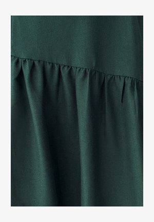 Tumši zaļš audums ar gludu tekstūru, kas izceļas ar savilktu dizainu jostasvietā, veidojot plūstošu siluetu.