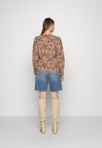Blusa a maniche lunghe, decorata con un motivo nei toni caldi, abbinata a pantaloni corti di jeans. Gli stivali alti fino al ginocchio, color crema e con un tacco spesso, completano il look.