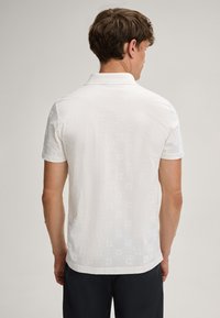 Witte polo met een gestructureerd patroon, korte mouwen en een klassieke kraag. De stof heeft een subtiele glans en fijne details.
