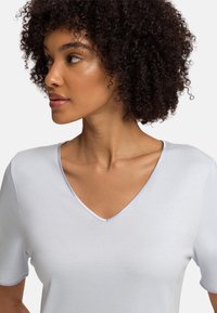 Bílý tričko s véčkovým výstřihem a krátkými rukávy, s hladkým povrchem a kontrastním světle modrým lemem kolem výstřihu.