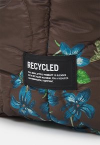 Återvunnet tyg med en brun bas dekorerad med blå blommönster. En svart etikett identifierar det som en hållbar produkt.