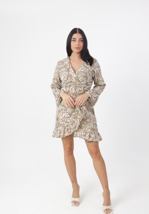 Robe portefeuille à motifs floraux marron avec des manches longues, un ourlet volanté et un décolleté en V. Portée avec des sandales blanches à bout ouvert.
