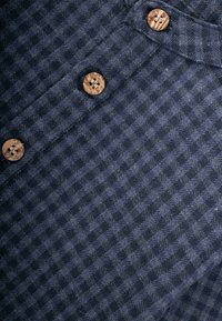 Tessuto blu navy con un motivo houndstooth texturizzato, caratterizzato da bottoni in legno naturali. La vista ravvicinata mette in evidenza i dettagli della trama e del design dei bottoni.