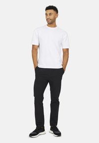 Witte katoenen T-shirt, korte mouwen, gecombineerd met zwarte taps toelopende broek en zwarte sportschoenen, met een minimalistisch ontwerp.