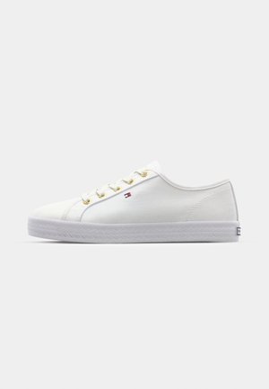 White canvas sneaker with round toe, white rubber sole, gold eyelets, and small logo patch. Smooth texture and simple design.
