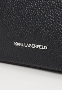 Borsa in pelle blu con texture e logo in maiuscolo "KARL LAGERFELD" in argento. Il primo piano mostra i dettagli della superficie goffrata e il design elegante.