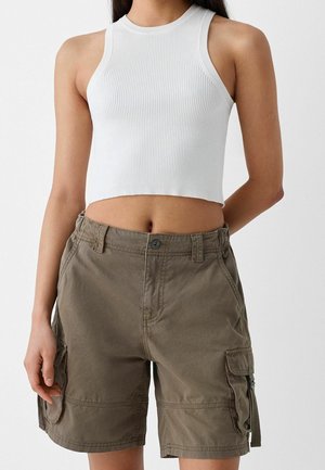 Femme portant un crop top blanc sans manches en maille côtelée et un short cargo vert olive, debout avec une main le long du corps.