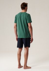 Zielona bawełniana koszulka z krótkim rękawem zestawiona z granatowymi szortami z delikatnym białym wzorem. Model pokazany z tyłu.