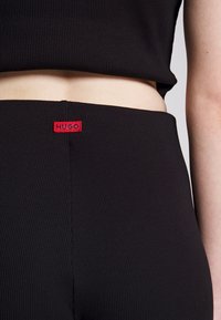 Zwarte geribbelde crop top gecombineerd met bijpassende high-waisted broek, met een rood "HUGO" logo label op de tailleband.