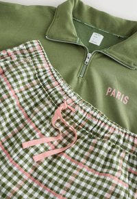 Green zippered sweatshirt with "PARIS" in light pink, paired with green and white checkered shorts featuring pink accents and an elastic waistband.