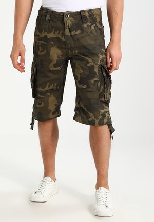 Homme portant un short cargo camouflage vert et marron longueur genou avec plusieurs poches et des baskets blanches.