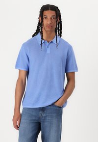 Lyseblå kortermet polo skjorte med et strukturert strikkemønster, med flat krage og to-knappers placket. Brukt med jeans.