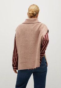 Stickad rosa väst med hög krage, med en texturerad yta och en avslappnad passform, bärs över en vinröd randig skjorta.