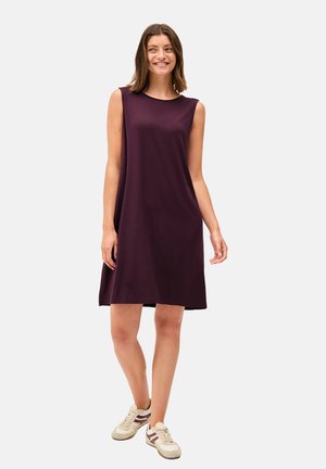 Robe sans manches de couleur violette avec une coupe décontractée, décolleté rond, mi-longue. Portée avec des baskets légères, avec des accents crème et bordeaux.