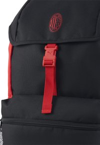 Zaino nero con accenti rossi, dotato di logo, tracolla regolabile e tasca con cerniera. Realizzato in tessuto resistente con una finitura testurizzata.