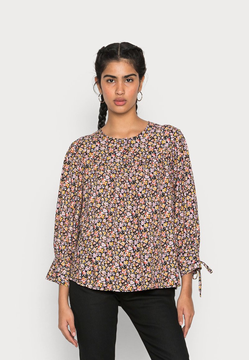 Blusa floral com um fundo preto adornado com pequenas flores em rosa, amarelo e branco, mangas longas com detalhes em laço e um decote redondo.