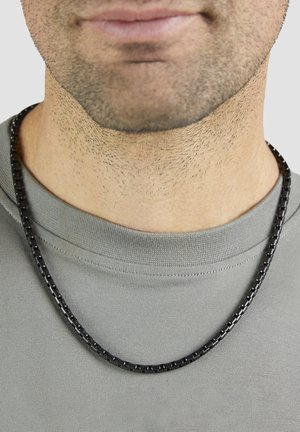 Schwarze Kettenhalskette, getragen von einer Person, mit glatter, glänzender Oberfläche und quadratischen Gliedern, liegend auf einem grauen Shirt.