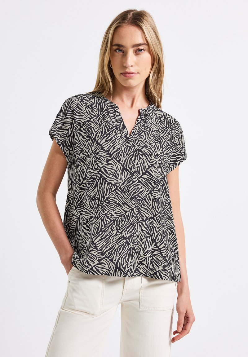 Top corto a maniche corte nero e beige con scollatura a V, caratterizzato da un motivo geometrico a zebra su un tessuto leggero.