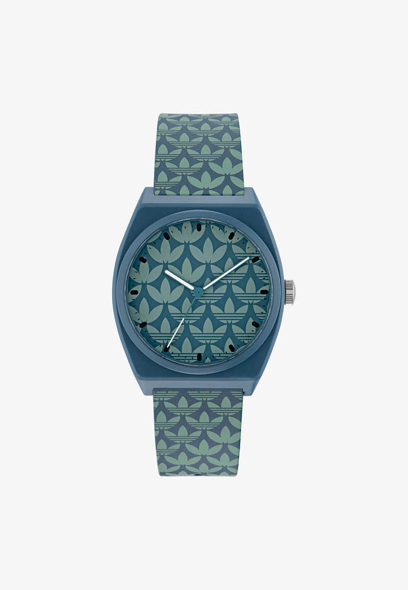 Blaues Armband mit sechseckigem Gehäuse, gemustertem Zifferblatt mit hellgrünen Formen und passendem strukturiertem Armband. Silberner Krone an der Seite.