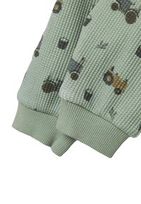 Dziecięce jasnobrązowe spodnie z dzianiny wafelowej z mankietami, z nadrukiem ciągników i motywami z farmy w stonowanych kolorach.