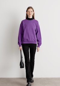 Felpa viola con scollo a girocollo, polsini e fondo a costine; abbinata a pantaloni neri aderenti e una piccola borsa nera.