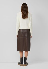 Pull en maille crème avec des manches texturées, jupe midi en cuir marron, et bottines noires avec des semelles épaisses et des accents en maille.