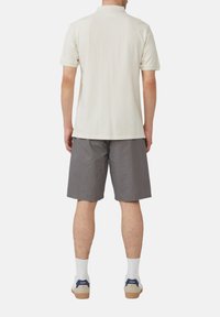 Hellbeige Polohemd mit kurzen Ärmeln, kombiniert mit grauen Shorts, weißen Socken und lässigen Sneakern, von hinten betrachtet.
