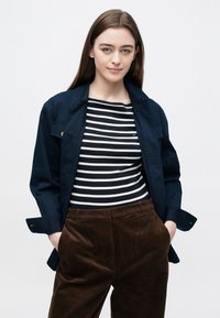Námornícka modrá bunda cez čierno-bielu pruhovanú blúzku, kombinovaná s hnedými kordurovými nohavicami. Hladké textúry a voľný strih po celej dĺžke.