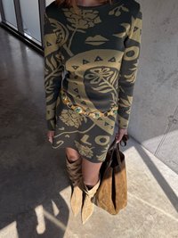 Pletaná dlhá sukňa s dlhým rukávom v tmavozelenej farbe s kvetinovým vzorom; zlatý opasok so zelenými akcentmi; hnedé semišové čižmy po kolená; hnedá taška.