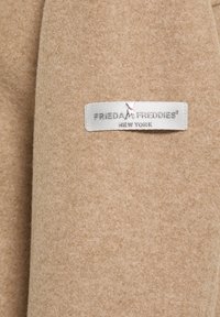 Beige wollen stofmix met een zachte textuur, voorzien van een zilveren label met de tekst "FRIEDA FREDDIES NEW YORK."