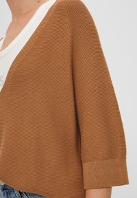 Brun stickad tröja med V-ringning, ribbade cuffs och texturerad tyg. Designen har en avslappnad passform och lätt material.