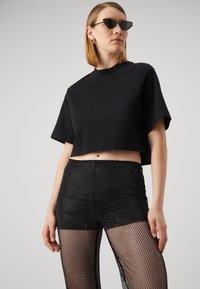 T-shirt nera corta con maniche corte e scollatura rotonda abbinata a leggings in rete nera lucida con pois argentati.