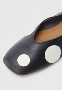 Zwarte leren platte schoen met een vierkante neus, voorzien van grote witte polka dots en een beige interieur. Glad oppervlak met minimale stikseldetails.