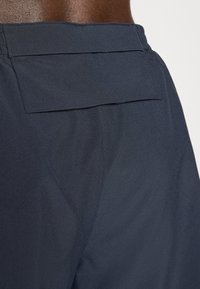 Navy blue shorts made of smooth fabric, featuring a back pocket with a flap and a fitted waistband, showcasing clean lines and minimalist design.