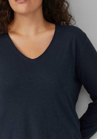 Marinefarbener Longsleeve mit V-Ausschnitt aus einem strukturierten Stoff, der eine lässige Passform und dezente Rippungen am Halsausschnitt aufweist.
