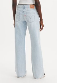 Jean large bleu clair en denim, avec un design classique à cinq poches et une étiquette en cuir sur la taille arrière.