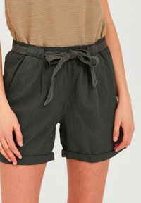 Pantaloni corti neri in lino con vestibilità ampia, vita elastica e una cintura in tessuto. Presentano risvolti sulle maniche e tasche laterali. Superficie testurizzata.