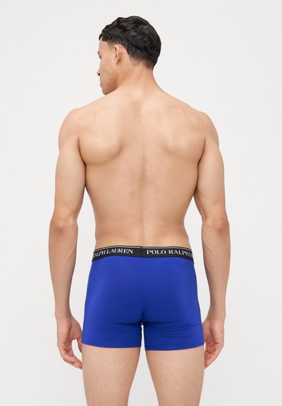 Boxeri albaștri cu un elastic negru inscripționat "POLO RALPH LAUREN", textură netedă și design ajustat. Pielea expusă pe partea superioară a corpului.