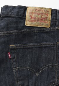 Poche arrière d'un jean Levi's bleu foncé avec coutures jaunes, étiquette rouge Levi's et écusson en cuir indiquant la taille W32 L32.
