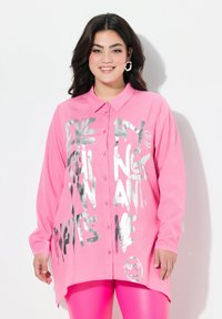 Rosa Langarmhemd mit Kragen und silbernem Graffiti-Text, mit einem Smiley-Grafik und asymmetrischem Saum.