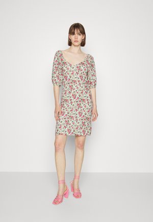 Vestido floral com mangas bufantes, apresentando padrões em rosa e verde sobre um fundo claro. Combinado com sandálias de salto alto, com tiras, na cor rosa.