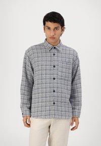 Blå og hvit rutete skjorte med knapper i et strukturert stoff, med krage og mørke knapper, sammen med lyse bukser.