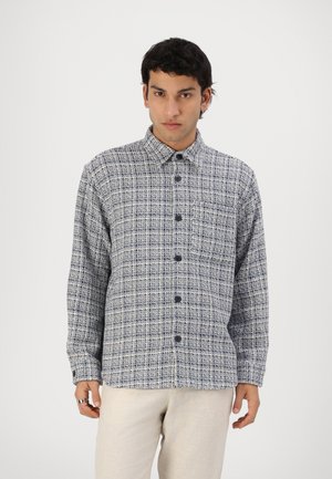 Blå og hvit rutete skjorte med knapper i et strukturert stoff, med krage og mørke knapper, sammen med lyse bukser.