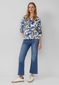 Haut à motif floral en blanc, marine et beige, associé à un jean évasé bleu. Les chaussures présentent des accents crème et marron.