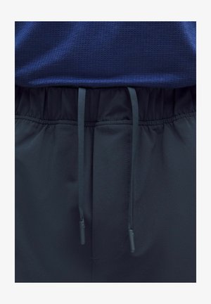 Granatowe spodnie sportowe z elastycznym pasem i czarnymi sznurkami, na ciemnoniebieskiej teksturowanej koszuli.