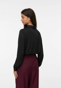 Zwarte blouse met lange mouwen en kraag, gladde textuur, gecombineerd met bordeauxrode hoge taille broek, die een ontspannen pasvorm en drapeervorm toont.