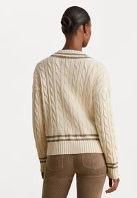 Kremowy sweter w warkocze z ribbowym wykończeniem u dołu i na mankietach, z brązowymi paskami w okolicy kołnierza i u dołu. Miękka tekstura i luźny krój.