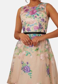 Vyšívané šaty s průhledným květinovým přehozem v béžové barvě, s fialovými a zelenými akcenty, s přiléhavým živůtkem a černým pasem.