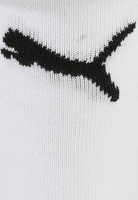 Biela ponožka s rebrovanou textúrou, ktorá má na boku výrazné vyšívané čierne logo Puma.